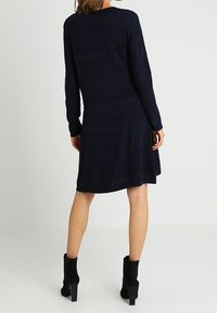 Abito blu navy a linea ad A con maniche lunghe, tessuto texturizzato, orlo all'altezza del ginocchio, abbinato a stivali neri alla caviglia. Design semplice e strutturato.