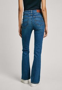 Blå denimflared jeans med en medelhög midja, synliga sömmar och en brun läderlapp på baksidan, med två bakfickor.