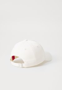 Witte pet van katoen, met een gebogen klep, verstelbare band aan de achterkant en een klein rood label binnenin de opening.