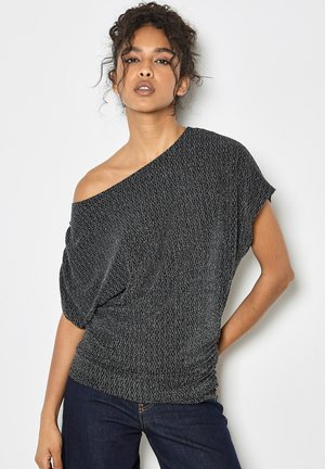 Asymetryczna czarna bluzka z srebrnymi detalami, teksturowany materiał, krótkie rękawy. Noszona z ciemnoniebieskimi dżinsami, prezentującymi luźny krój.