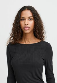 Black ribbed long-sleeve top with a boat neckline. The fabric features a textured pattern, and the design is fitted around the torso.