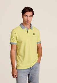 Polo en coton jaune vif avec un col gris et des accents bleus. Manches courtes et un petit logo sur la poitrine.