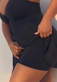 Schwarzes Schwimmbadkleid mit tailliertem Oberteil und fließendem Rock. Glatte Textur, verstellbare Träger und ein mehrlagiges Design für eine dezente Abdeckung.