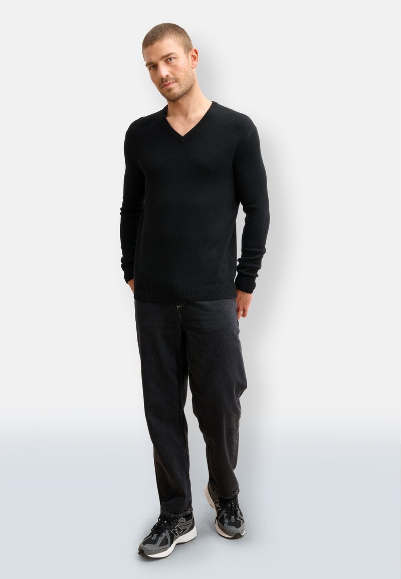 Suéter negro de pico hecho de material suave, combinado con pantalones negros holgados y zapatillas deportivas negras. Diseño simple y limpio con puños acanalados.