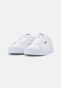 Vit sneaker med slät läderöverdel, rund tå, snörning framtill och prägling av "TOMMY JEANS"-logotypen på den tjocka gummisulans.