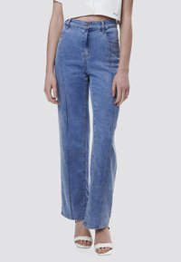 Vaqueros de tiro alto en azul claro con un diseño de pierna ancha, que presentan bolsillos frontales y costuras en contraste. El material parece denim con una textura suave.