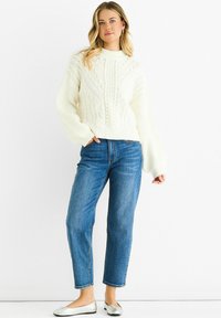 Cream cable-knit sweater with ribbed cuffs, paired with straight-leg blue jeans and silver ballet flats.