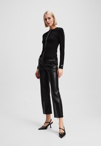 Zwarte langemouwen top met een witte ritssluiting aan de voorkant, gecombineerd met zwarte leren cropped broek met ritssluitingen bij de enkels en zwarte hoge hakken.