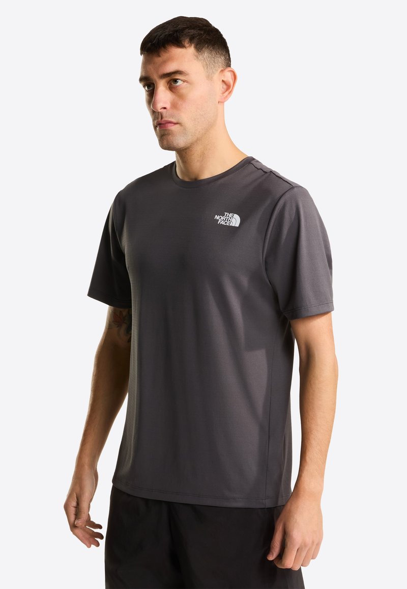 T-shirt de sport gris foncé à manches courtes avec un col rond et un logo sur le côté gauche de la poitrine. Texture lisse, tissu léger, coupe décontractée.