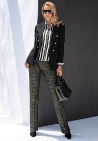 Schwarzer Blazer mit silbernen Knöpfen über einem gestreiften Shirt, kombiniert mit strukturierten schwarz-weißen Hosen und einer schwarzen, gesteppte Handtasche.