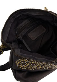 Schwarze Lederhandtasche mit strukturiertem Finish, ausgestattet mit einem Reißverschluss, Innenfächern und dekorativen gold- und silberfarbenen Nieten entlang der Vorderseite.