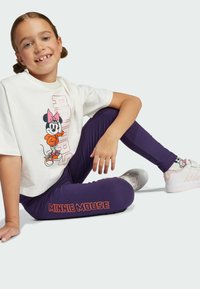 Vit kortärmad t-shirt med en grafik av Minnie Mouse, kombinerad med lila leggings märkta "MINNIE MOUSE" i orange. Lätta sneakers med rosa detaljer.