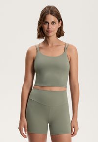 Világoszöld sportöltözet, amely egy vékony pánttal rendelkező cropped tank topból és sima, rugalmas anyagú, magas derekú sortból áll.