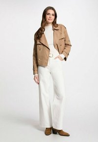 Chaqueta corta beige con botones dobles, combinada con un suéter crema acanalado y pantalones de pierna ancha blancos. Botas de tacón marrón completan el look.