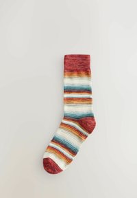 Viacfarebná ponožka s červeným lemom, so zvislými pruhmi v modrej, oranžovej a krémovej, vyrobená z mäkkého, textúrovaného materiálu.