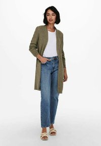 Cardigan a maglia verde oliva con maniche lunghe, apertura frontale, abbinato a una t-shirt bianca e jeans blu a gamba dritta. Indossato con sandali chiari.