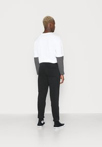 Hvit t-skjorte med svarte og hvite stripete langermede ermer, parret med svarte joggebukser. Svarte høyhælte sneakers fullfører antrekket.