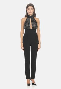 Tuta nera con scollo all'americana, con un corpetto testurizzato e decorato con perline e pantaloni attillati con pieghe. Tacchi neri chiusi.