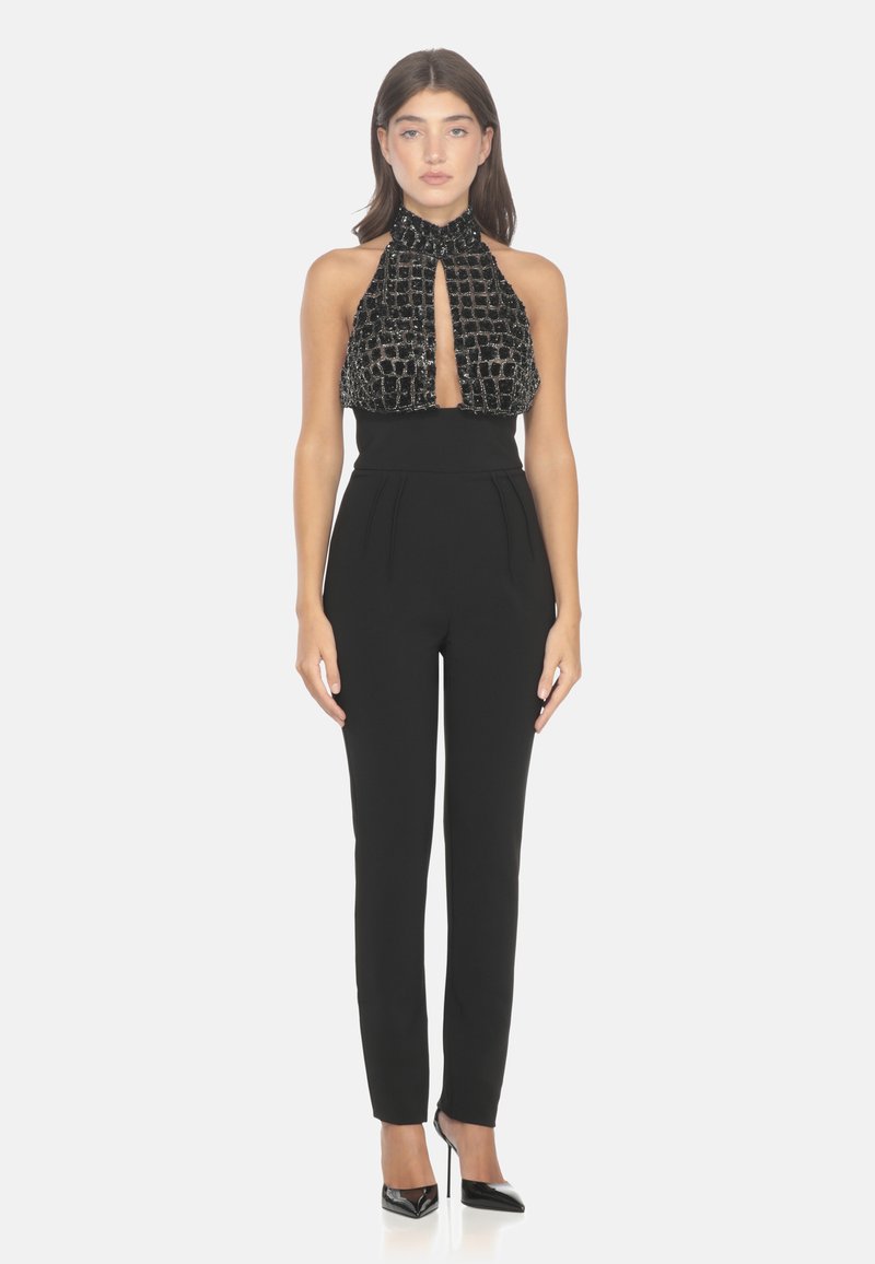 Tuta nera con scollo all'americana, con un corpetto testurizzato e decorato con perline e pantaloni attillati con pieghe. Tacchi neri chiusi.