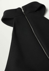 Vêtement noir en tissu lisse, doté d'un col montant et d'une fermeture éclair argentée sur un côté. Conception simple et structurée sans motifs apparents.