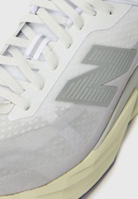 Pantofii sport gri deschis, cu un superior din plasă texturată, șireturi plate, talpă din cauciuc și accente reflectorizante prominente, având un logo mare gri.