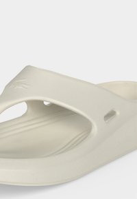 Μινιμαλιστικό υπόλευκο σανδάλι που φοριέται εύκολα, με φαρδιά λουράκι, οπές αερισμού και υφασμένο πάτο για άνεση.