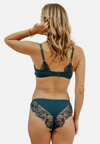 Soutien-gorge en teal et culottes assorties en tissu lisse avec des accents de dentelle florale noire. Bretelles ajustables et fermeture à crochets à l'arrière.