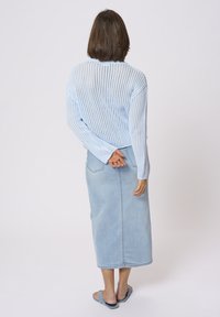 Light blue knitted sweater with a loose fit, paired with a long light denim skirt and flat sandals. The back view shows a relaxed style.