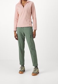 Ljusrosa fleece-tröja med dragkedja, ihop med gröna cargobyxor med fickor. Skorna är flerfärgade vandringsskor.