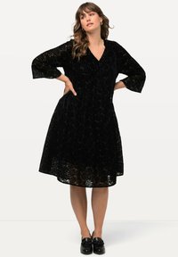 Abito in pizzo nero con scollo a V, maniche a tre quarti e gonna a ruota, decorato con un motivo floreale e una texture a strati.