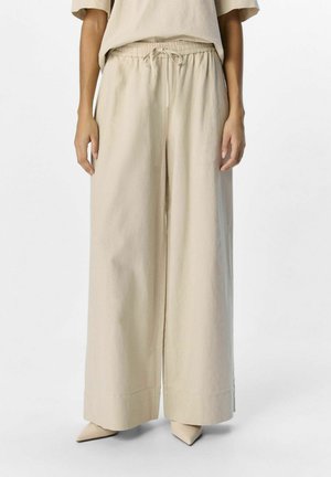 Pantalons beige à jambes larges en tissu léger, dotés d'une taille élastique avec cordon de serrage et d'une finition lisse et texturée.