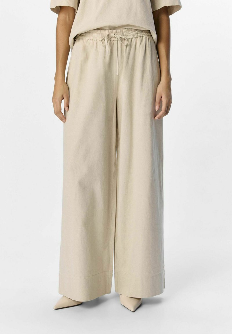 Pantalons beige à jambes larges en tissu léger, dotés d'une taille élastique avec cordon de serrage et d'une finition lisse et texturée.