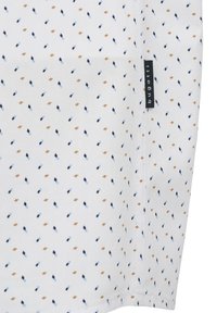 Weißer Stoff mit einem Rautenmuster in Blau, Marineblau und Braun. Mit einem kleinen schwarzen Etikett mit "b nud" am Rand.