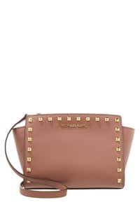 Růžová kožená kabelka je zdobena zlatými pyramidovými hroty podél okrajů, má horní zip a ramenní popruh. Zahrnuje branding Michael Kors.
