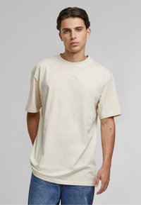 Cremefarvet kortærmet t-shirt i blødt stof med et lille hvidt broderet logo på brystet og en afslappet pasform.