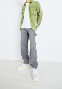 Chaqueta de camisa de pana verde, camiseta blanca, vaqueros de pierna ancha grises y zapatillas gris claro con suelas blancas. Conjunto informal mostrado desde la cintura hacia abajo.