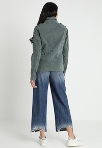 Groene, lichte, lange mouwen jack met een ontspannen pasvorm en verstelbare koord in de taille. Gecombineerd met wijd uitgeslagen, vervaagde blauwe jeans en sneakers.