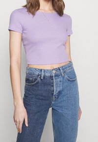 Levandulový žebrovaný crop top s krátkými rukávy v kombinaci s dvoubarevnými džínami, které mají na jedné straně světlejší modrou a na druhé tmavší modrou.