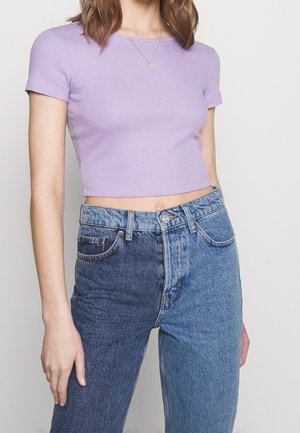 Lila ribbed crop top met korte mouwen, gecombineerd met twee tinten denim jeans, met aan de ene kant een lichtere blauwe kleur en aan de andere kant een donkerder blauwe kleur.