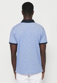 Blå pikétröja med en strukturerad yta, som har en marinblå krage och små geometriska mönster över hela. Korta ärmar med marinblå accenter.