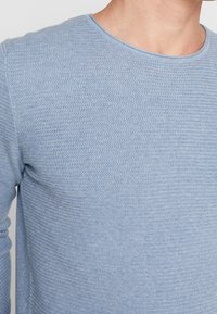 Ljusblå stickad tröja med rund halsringning, med ett strukturerat mönster, långa ärmar och en figurnära silhuett.