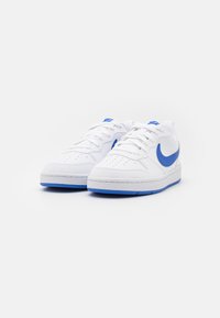 White sneakers with blue accents, featuring a textured leather upper, perforations on the toe, and a blue rubber sole.