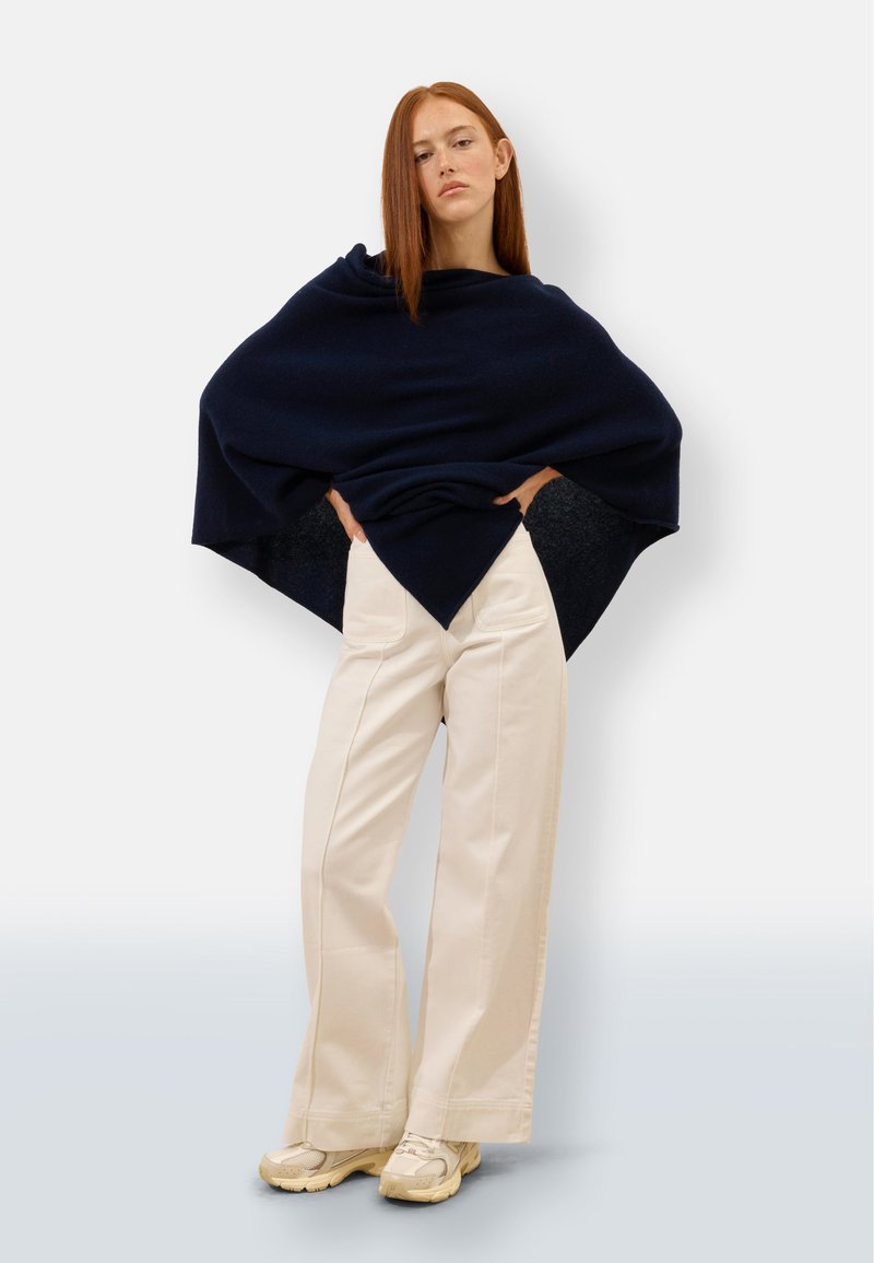 Granatowy dzianinowy poncho o trójkątnym kształcie, zestawione z kremowymi spodniami o szerokich nogawkach. Stylizacja charakteryzuje się miękką fakturą i luźnym krojem.