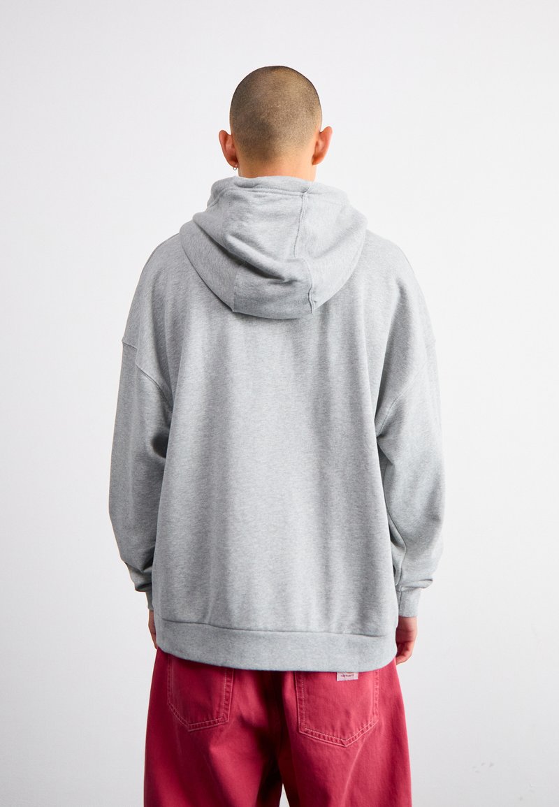Szara hoodie z luźnym krojem, ze ściągaczami przy rękawach i dole. Noszona z różowymi, luźnymi spodniami. Widok z tyłu pokazuje kaptur i ramiona.