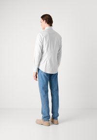 Langärmeliges, hellgraues Hemd mit Rückenpasse. Kombiniert mit lässigen blauen Jeans und beigen Schuhen. Einfaches Design, keine sichtbaren Muster.