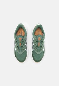 Green athletic shoes with a textured upper, white stripes, orange accents, and a cork insole. Features padded collar and lacing for secure fit.