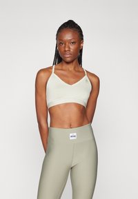 Sujeción deportiva verde claro con un diseño de escote en V, tirantes finos y detalle de logo. Combinado con leggings de tiro alto a juego y con canalé.