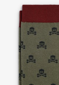 Calcetines verde oliva con un diseño estampado que presenta calaveras y huesos cruzados en negro. La parte superior tiene un puño rojo con textura acanalada.
