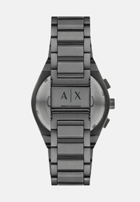 Sivi nehrđajući čelik sat s povezanim remenom, s okruglim kućištem i crnim logotipom na stražnjoj strani. Minimalni detalji i elegantan dizajn.