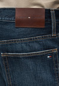 Σκούρο μπλε τζιν από denim με καφέ δερμάτινη ετικέτα Tommy Hilfiger και μικρή σημαία Tommy Hilfiger στη ραφή πίσω τσέπης.